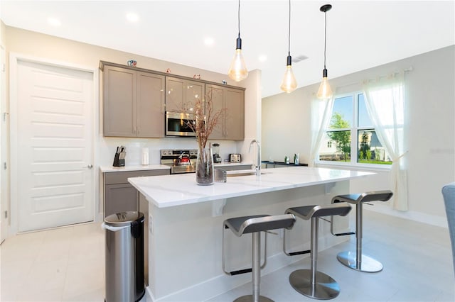 kitchen featuring light tile floors, hanging light fixtures, a center island with sink, stainless steel appliances, and a kitchen bar