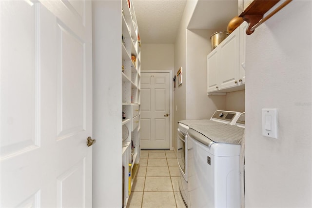 washroom with a textured ceiling, cabinets, washing machine and dryer, and light tile floors