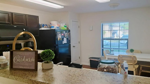 kitchen with light stone countertops, dark brown cabinets, and black appliances