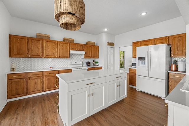 kitchen with dark hardwood / wood-style flooring, backsplash, white appliances, and a kitchen island