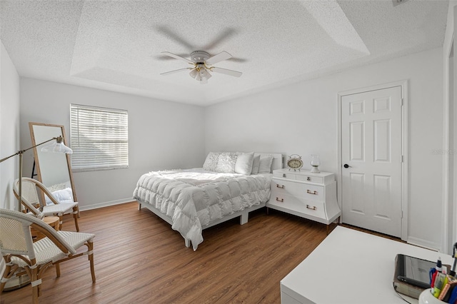 bedroom featuring dark hardwood / wood-style flooring, ceiling fan, a textured ceiling, and a raised ceiling