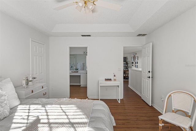 bedroom featuring ceiling fan, dark wood-type flooring, a tray ceiling, and ensuite bath