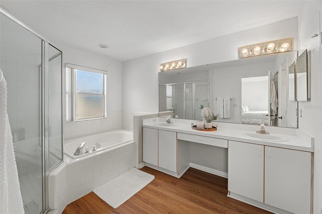 bathroom featuring independent shower and bath, double vanity, hardwood / wood-style floors, and a textured ceiling