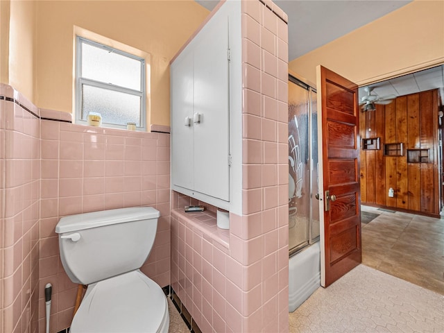 bathroom featuring toilet, ceiling fan, tile walls, combined bath / shower with glass door, and tile flooring