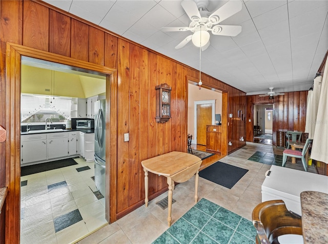 interior space with light tile flooring, ceiling fan, wood walls, and sink