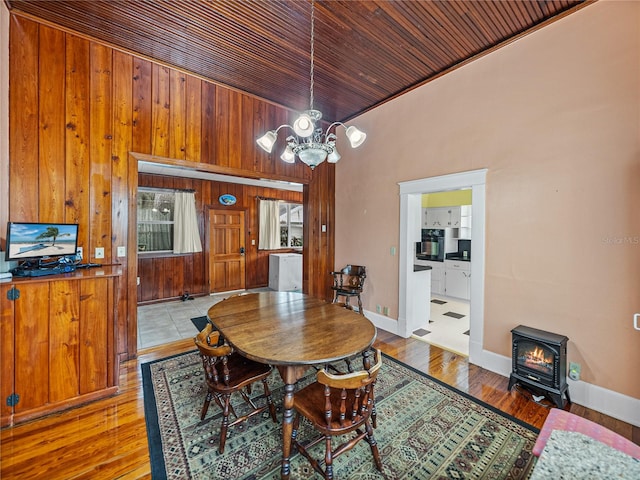 dining space featuring a notable chandelier, wood walls, a wood stove, and light hardwood / wood-style flooring