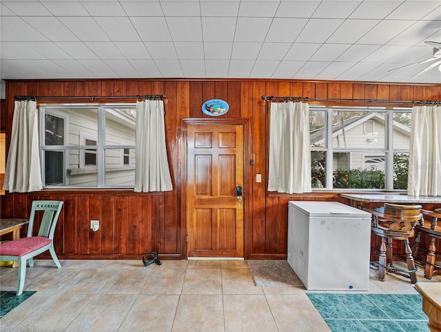 interior space with wooden walls, ceiling fan, and light tile floors