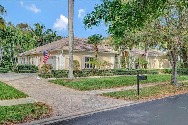 view of front of house featuring a garage, a tiled roof, decorative driveway, a front yard, and stucco siding