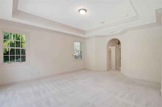 empty room featuring arched walkways, light carpet, a raised ceiling, and baseboards