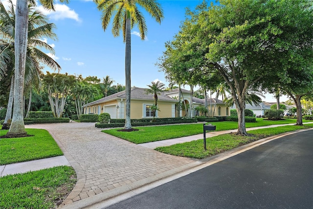 single story home with stucco siding, an attached garage, decorative driveway, and a front yard
