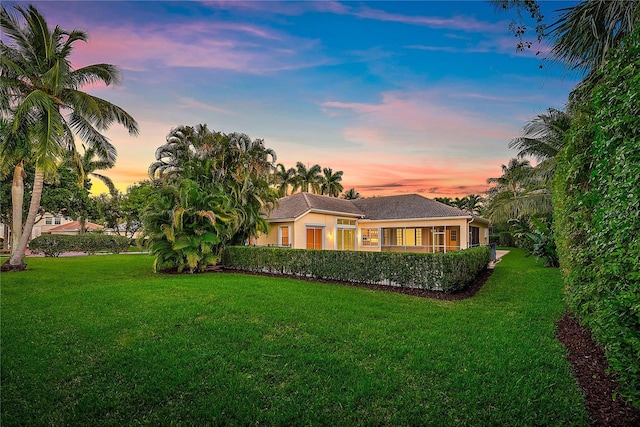 back of property at dusk with a lawn and stucco siding