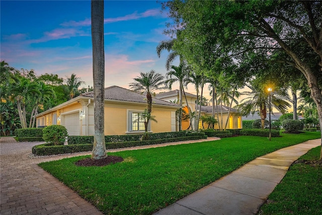view of front of property with a garage, a front yard, decorative driveway, stucco siding, and a tiled roof