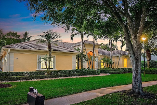 mediterranean / spanish house featuring a lawn, a tile roof, and stucco siding