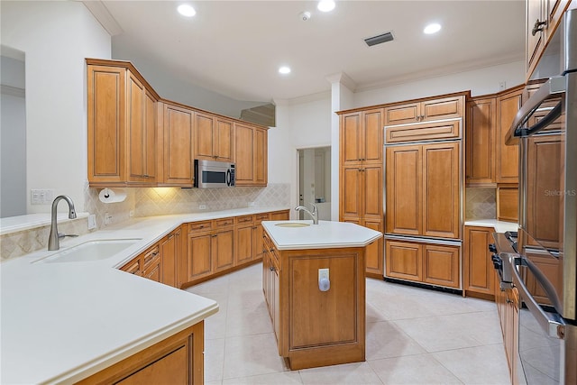 kitchen featuring a sink, ornamental molding, stainless steel microwave, and a center island with sink