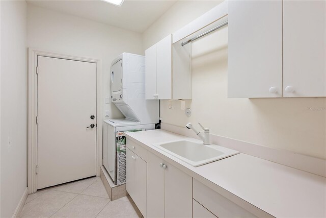 clothes washing area featuring stacked washer / drying machine, cabinet space, a sink, baseboards, and light tile patterned flooring