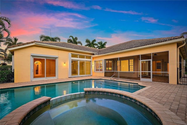 back of house at dusk with a pool with connected hot tub, a tile roof, a sunroom, and stucco siding