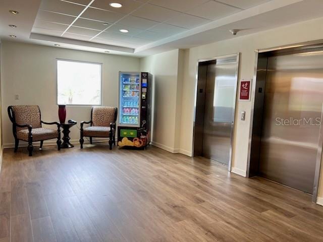 living area featuring a tray ceiling, hardwood / wood-style floors, and elevator