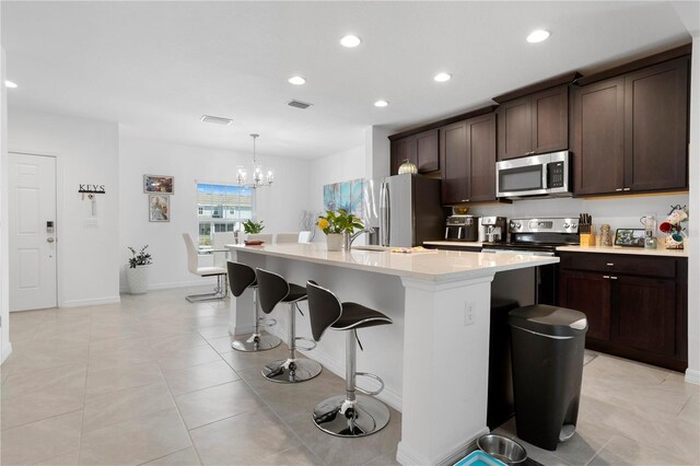 kitchen with an island with sink, stainless steel appliances, a notable chandelier, decorative light fixtures, and a kitchen breakfast bar