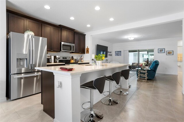 kitchen with a kitchen bar, appliances with stainless steel finishes, a kitchen island with sink, and dark brown cabinetry