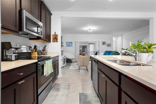 kitchen with light stone countertops, appliances with stainless steel finishes, sink, light tile floors, and dark brown cabinetry