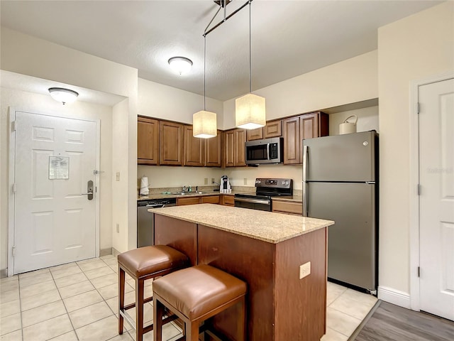 kitchen featuring pendant lighting, light stone counters, appliances with stainless steel finishes, a breakfast bar area, and a center island