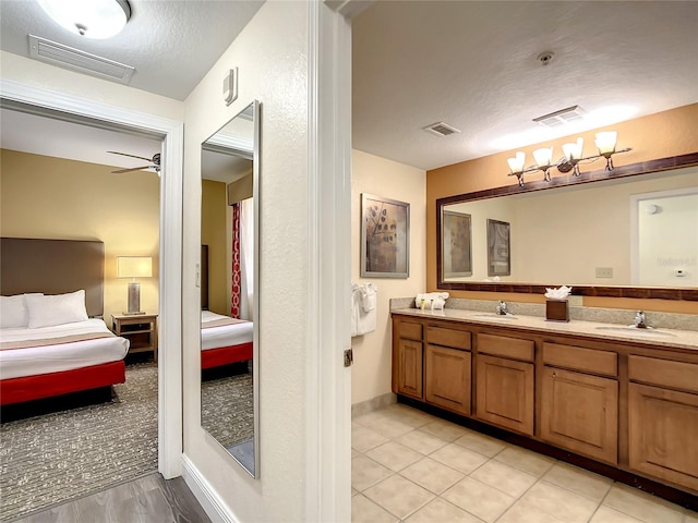 bathroom featuring oversized vanity, a textured ceiling, ceiling fan with notable chandelier, dual sinks, and tile floors