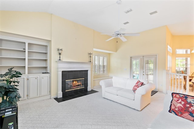 living room with ceiling fan, french doors, a tile fireplace, light colored carpet, and high vaulted ceiling