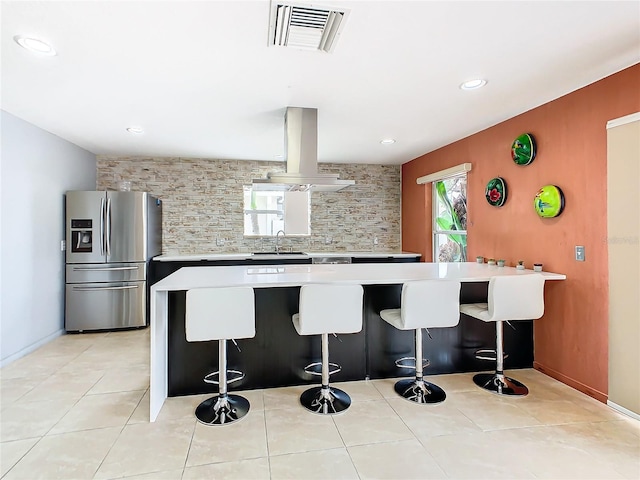 kitchen featuring stainless steel fridge, a kitchen breakfast bar, wall chimney exhaust hood, sink, and tasteful backsplash