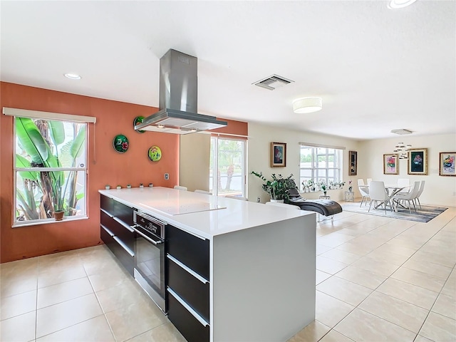 kitchen featuring black electric cooktop, light tile floors, a center island, stainless steel oven, and island range hood