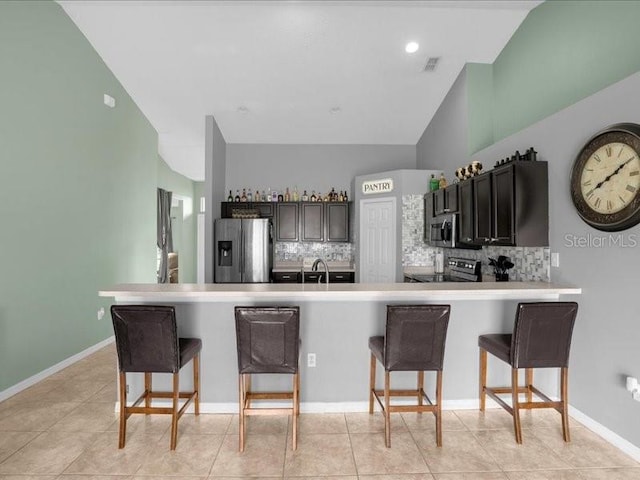 kitchen with light tile patterned flooring, a kitchen breakfast bar, appliances with stainless steel finishes, decorative backsplash, and kitchen peninsula