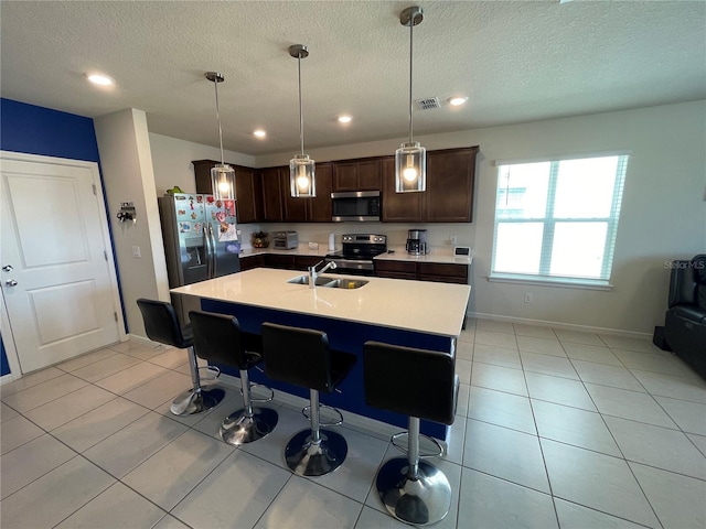 kitchen featuring stainless steel appliances, decorative light fixtures, a center island with sink, dark brown cabinets, and sink