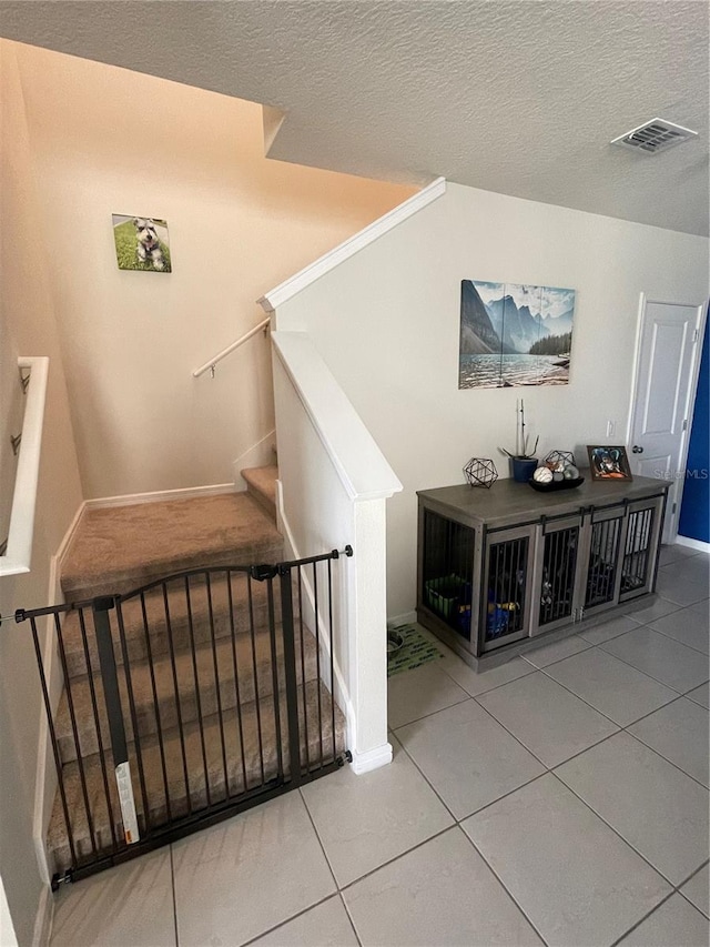 stairway with a textured ceiling and light tile floors