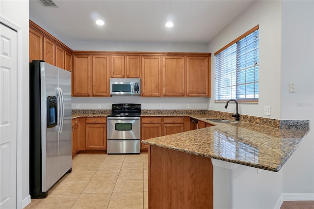 kitchen with light tile patterned flooring, appliances with stainless steel finishes, sink, dark stone countertops, and kitchen peninsula