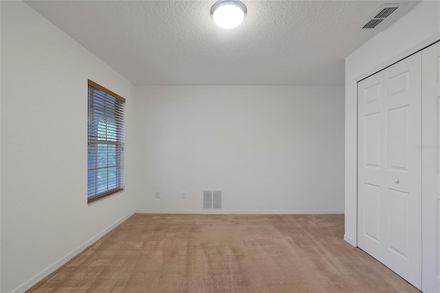 unfurnished bedroom featuring light colored carpet, a textured ceiling, and a closet