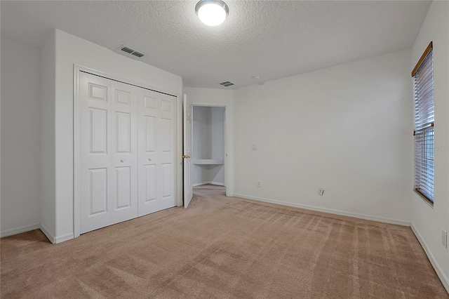 unfurnished bedroom featuring light carpet, a closet, and a textured ceiling