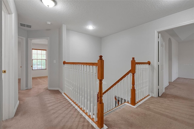 hallway with light carpet and a textured ceiling