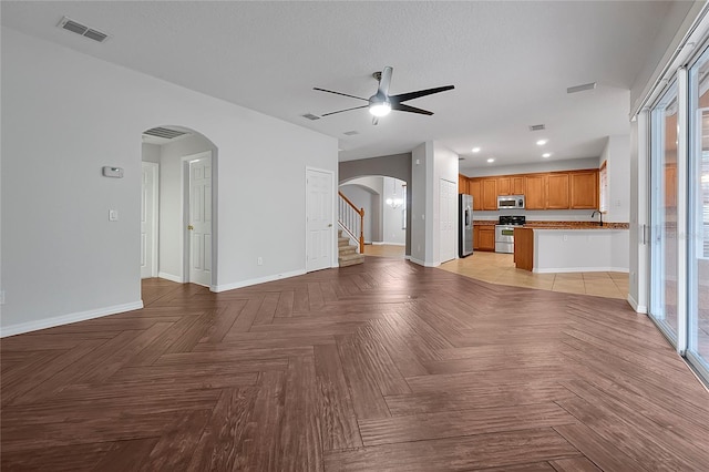 unfurnished living room featuring light parquet flooring, a textured ceiling, and ceiling fan