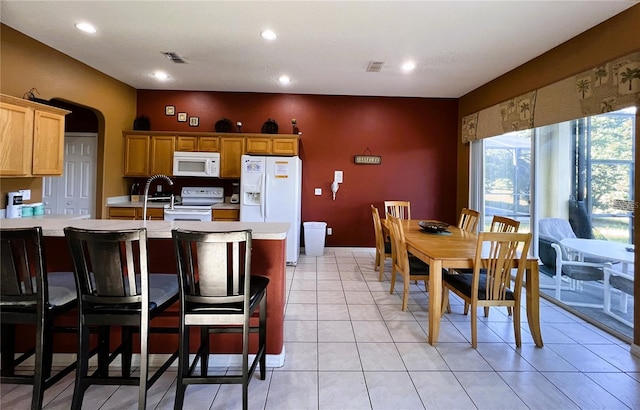 kitchen with a breakfast bar area, white appliances, and light tile floors