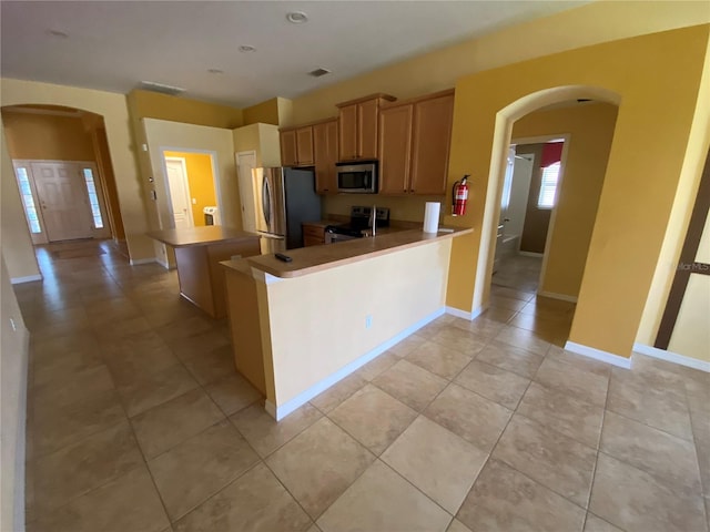 kitchen with kitchen peninsula, light tile patterned floors, stainless steel appliances, and a breakfast bar area