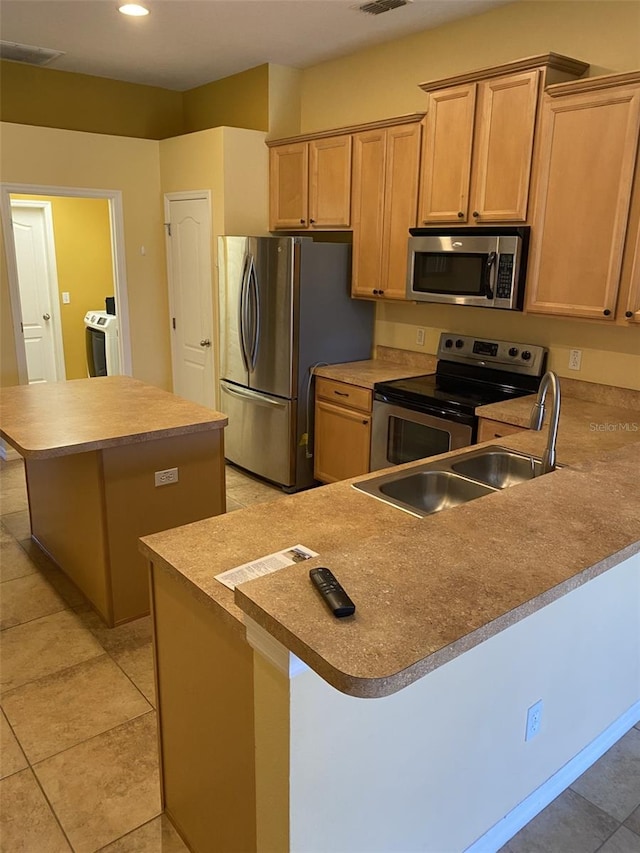 kitchen featuring light tile patterned floors, a kitchen island, kitchen peninsula, stainless steel appliances, and washing machine and clothes dryer