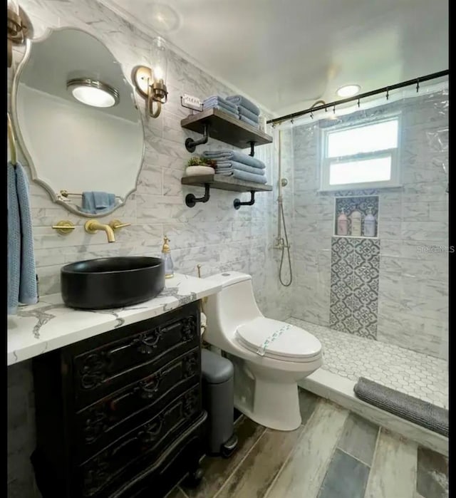 bathroom with tile walls, vanity, toilet, and tiled shower