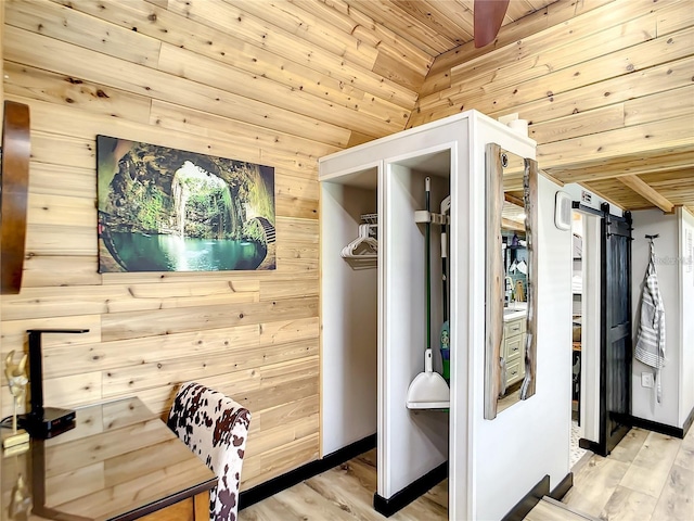 interior space featuring ceiling fan, a barn door, light hardwood / wood-style floors, wood ceiling, and wooden walls