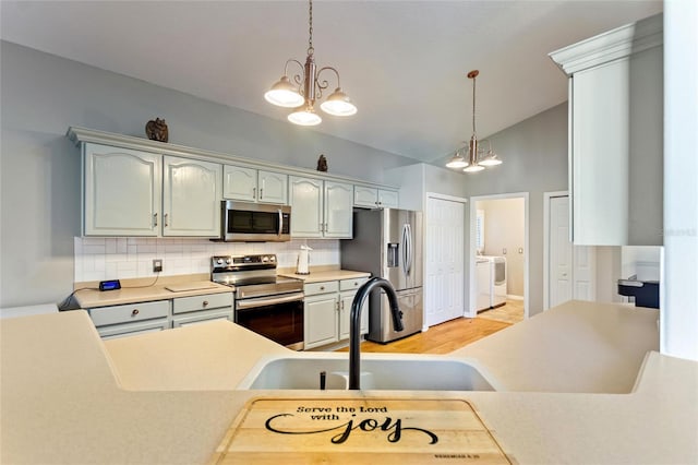 kitchen with washing machine and dryer, stainless steel appliances, light hardwood / wood-style floors, tasteful backsplash, and hanging light fixtures