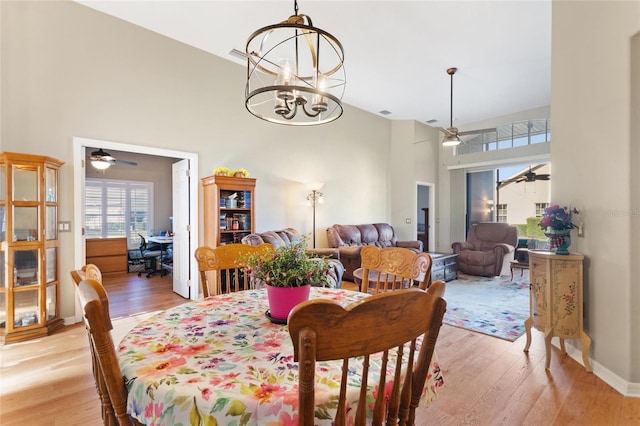 dining area featuring light hardwood / wood-style floors, a high ceiling, and ceiling fan with notable chandelier