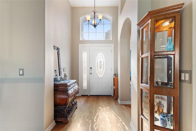 entryway with light hardwood / wood-style flooring, an inviting chandelier, and a towering ceiling