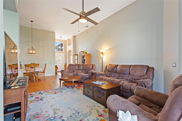 living room with high vaulted ceiling, light hardwood / wood-style floors, and ceiling fan with notable chandelier