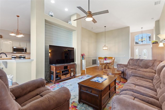 living room with ceiling fan with notable chandelier, light wood-type flooring, and a towering ceiling