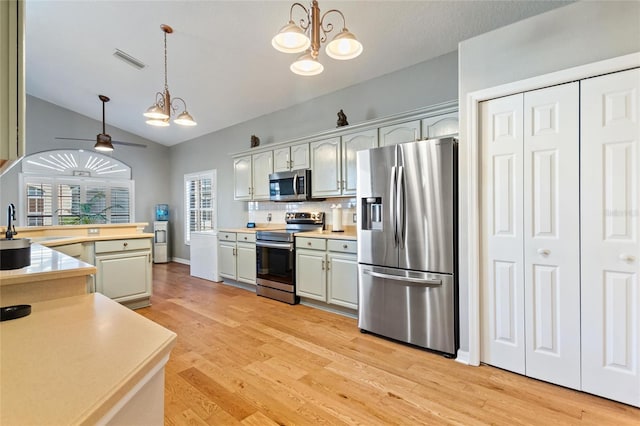 kitchen featuring stainless steel appliances, pendant lighting, lofted ceiling, light wood-type flooring, and ceiling fan with notable chandelier