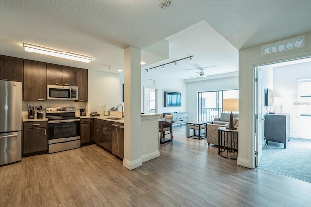 kitchen featuring rail lighting, ceiling fan, appliances with stainless steel finishes, and light hardwood / wood-style floors