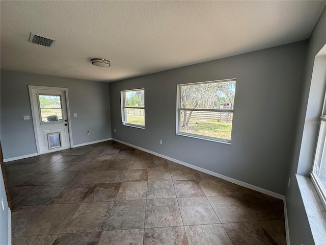 tiled empty room featuring plenty of natural light and a textured ceiling